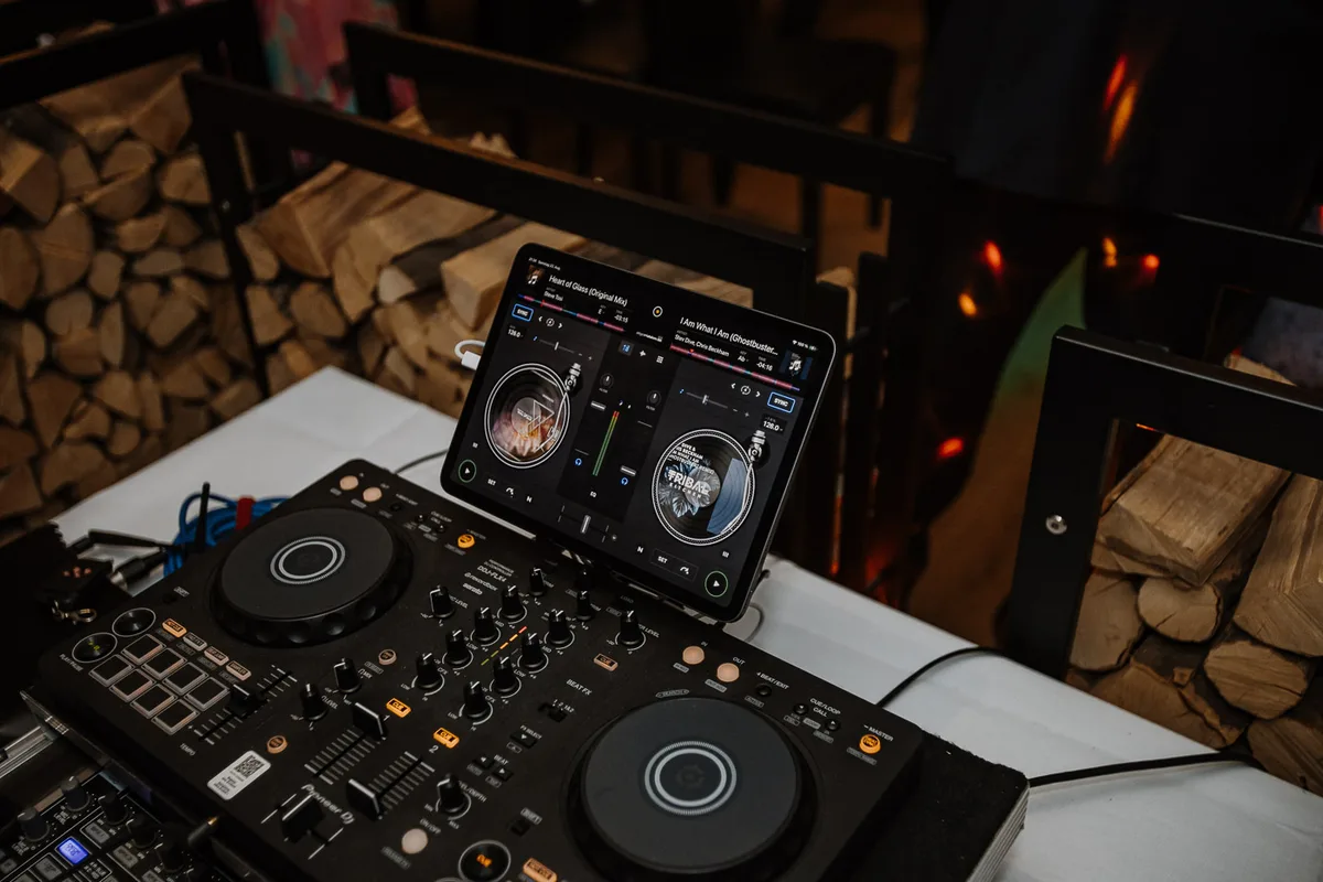 DJ-Setup mit Pioneer-Controller und iPad vor Brennholz-Wand am Abend