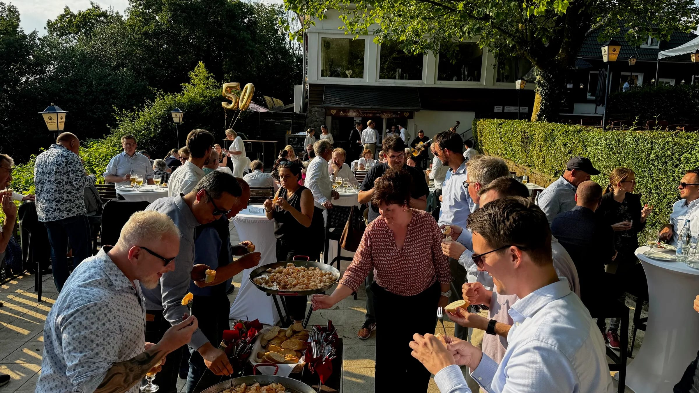 Outdoor-Sektempfang mit Gästen, Goldballons und Live-Musik auf der Terrasse