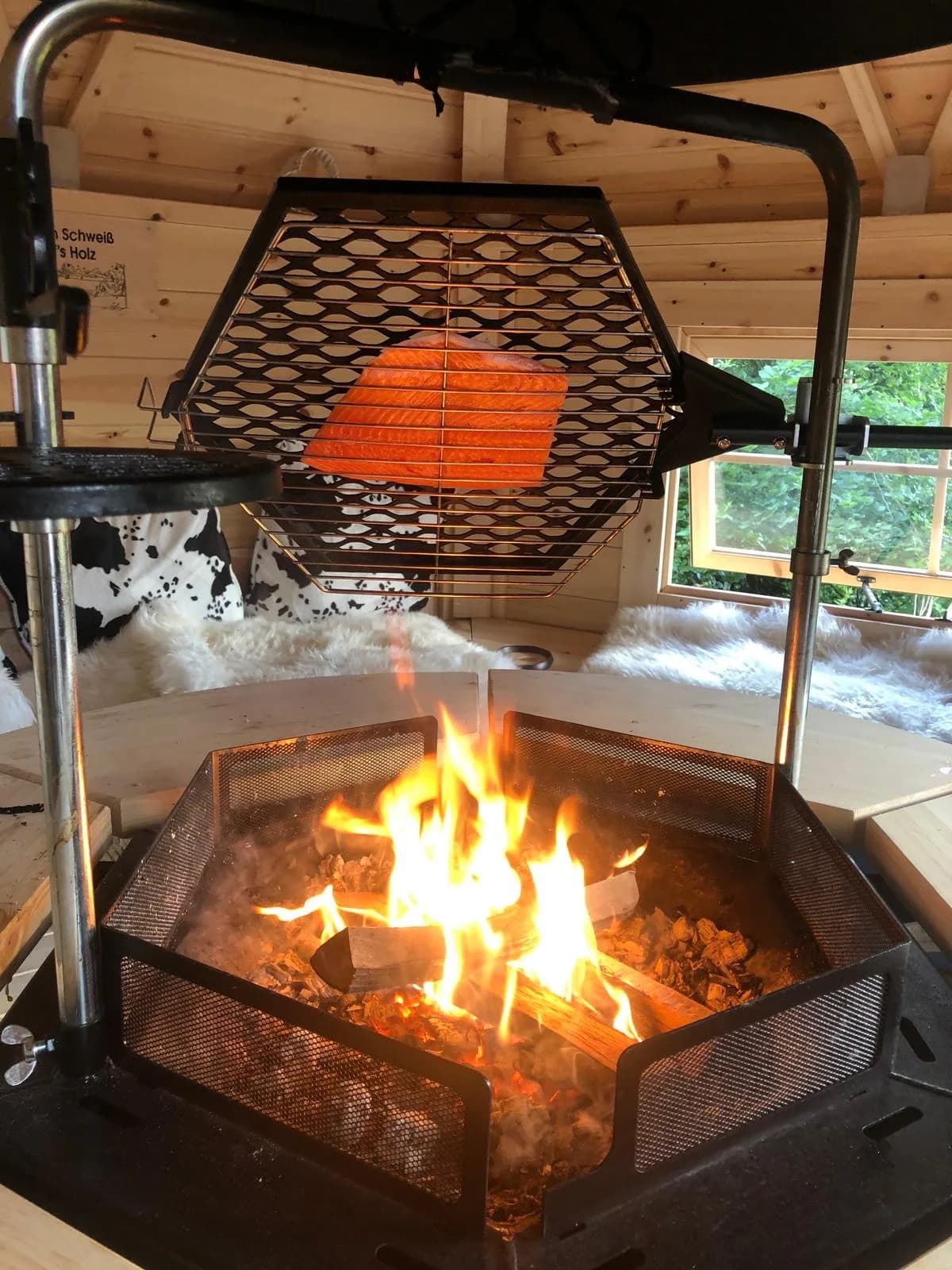 Innenraum der finnischen Grillkota mit offenem Feuer und Flammlachs auf dem Grillrost