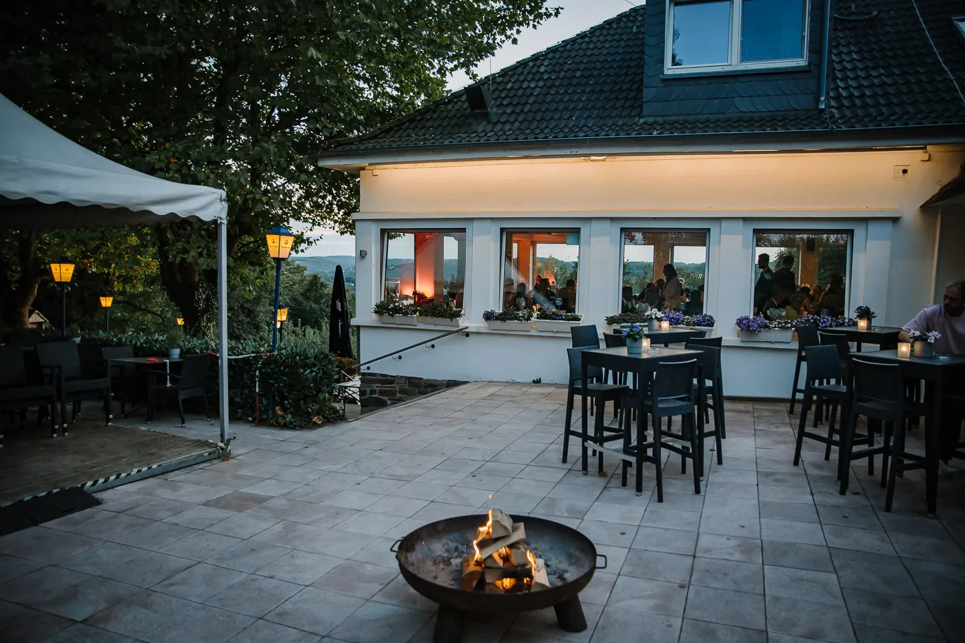 Feuerschale auf der Terrasse der Heimlichen Liebe am winterlichen Abend, warm erleuchtete Fenster im Hintergrund